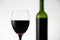 Blurry view of glass of red wine with bottle in the background. Wineglass full of alcohol drink on white background