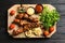 Board with barbecued meat, garnish and sauces on wooden background