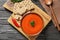 Board with bowl of fresh homemade tomato soup and crispbreads on wooden background