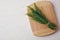 Board with bundle of fresh rosemary twigs on white wooden background. Space for text