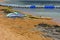 Board with a sail for windsurfing lessons is on a sandy beach next to the sea in the background of yellow sand.