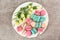 Board with tasty macarons and roses on grey background, top view