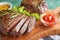 Board with tasty steaks, herbs and sauce on green background, closeup