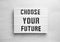 Board with words CHOOSE YOUR FUTURE on wooden background, top view. Career concept