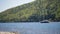 Boat empty-mast sailing against current of a river on background of slope mixed forest in a sunny day.