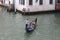 Boat, gondola with tourists and a gondolier that steers the boat, green water and old Venetian buildings