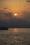 Boat on ocean, Bright sun in an orange sky with dark clouds at sunset