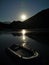 A boat with on the river on a moonlit night.  Moon, river and mountains at night.