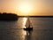 boat sailing on a lake across the path of a golden sunset with unidentifiable people in silhouette and swans swimming in the