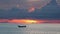 Boat in sea during sunset. Silhouette of small rowing boat floating on rippling water of calm sea during sundown in cloudy evening
