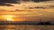 Boat silhouette crossing the ocean towards an orange sunset sky on the horizon.