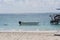 Boat tied to deck in shimmering water on sandy beach, with wispy blue sky in background