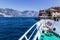 Boat tour: Boat bow, view over azure blue water, village and  mountain range. Lago di Garda, Italy