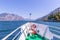 Boat tour: Boat bow, view over azure blue water, village and  mountain range. Lago di Garda, Italy