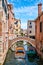 Boat under a bridge on a narrow canal sidelined by old buildings in Venice