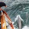 A Boater Points at Bottlenose Dolphins Riding the Bow Wave