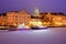 Boats on Frozen Trave river at nights. Lights on Lubeck city embankment.