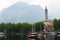 Boats on lake Como near church with tower, trees and mountain in background.