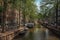 Boats moored at side of tree-lined canal, brick buildings and sunny blue sky in Amsterdam.