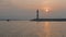 Boats passing lighthouse with rising sun at
