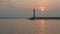 Boats passing lighthouse with rising sun at