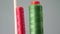 A bobbin of red and green cotton thread on the spindle of the sewing machine in the foreground, close-up. sewing factory