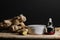 Body cream container and oil tube with ginger oil extract on wooden table with ginger roots and slices.