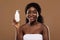 Body Skin Moisturising. Attractive Black Female In Towel Holding Bottle With Lotion