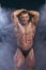 Bodybuilder man with a perfect muscle body on dark with smoke