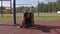 Bodybuilder sits on his knees of the sports ground with a disk from the barbell on the belt and and shakes her head from