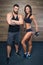 Bodybuilder with tattoo and beard and a smiling sporty girl are posing in a gym