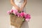 Boho girl holding pink peonies in straw basket. Stylish hipster woman in bohemian floral dress gathering peony flowers on white