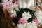 Boho girl holding pink and white peonies in hands at rustic wooden chair. Stylish hipster woman in bohemian dress arranging peony