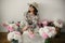 Boho girl sitting at pink and white peonies in rustic basket and metal bucket on wooden floor. Stylish hipster woman in bohemian