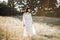 Boho girl in white dress, with feathers in hair and flash tattoos standing and looking away