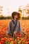 Boho stylish woman walking in red poppies meadow.