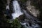 Boho woman wearing hat and poncho standing by the waterfall and looking at it