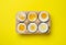 Boiled chicken eggs of different readiness stages in carton on yellow background, top view