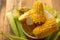 Boiled corn cob in a plate with butter, on wooden textures and green stalks of corn, tasty homemade food, for a picnic