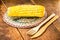 Boiled corn cob, on a rustic wooden table, with recycled wood graphs, bamboo forks