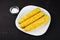 boiled corn on a white square plate, dark table, hodgepodge