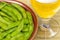 Boiled edamame in brown bowl with glass of beer