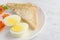 Boiled eggs, bread, carrots, and tomatoes on a white plate with a knife and fork