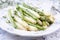 Boiled green and white Asparagus offered on a bone China porcelain plate on a well-laid table