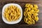 Boiled pasta conchiglie in plate, raw pasta on wooden table. Top view