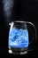 Boiling glass kettle with blue light on a black background, steam comes from the spout