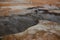 Boiling mudpots in the geothermal area Hverir and cracked ground around with unrecognisable tourists, Iceland in summer. Myvatn