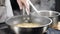 Boiling risotto in slow motion. White smoke rising above hot frying pan on dark background. Cooking in restaurant