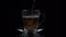 Boiling water is poured into a glass teacup where a portion of tea is poured, slow motion, on a black background