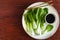 Bok choy served on a white plate and sauce on wood surface top view